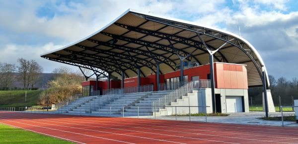 Tribüne mit überdachtem Zuschauerbereich und roter Tartanbahn.